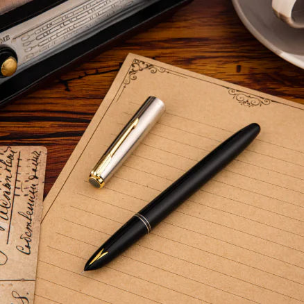 Black and gold fountain pen on a wooden surface with a notebook and vintage items.