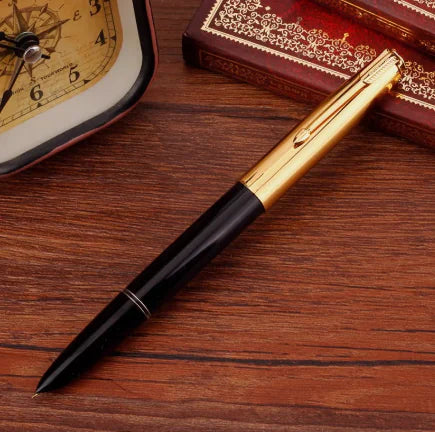 Gold and black pen on a wooden surface with an ornate book and clock in the background