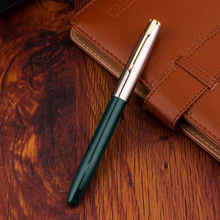 Green and gold pen on a wooden surface with a brown leather notebook.